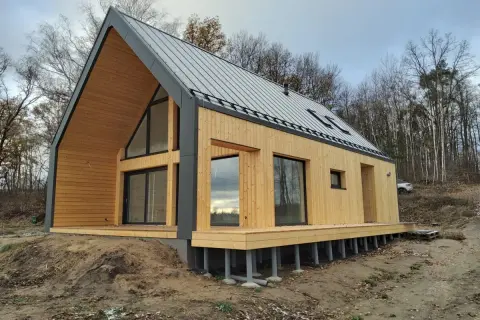 Nowoczesny dom modułowy z drewna i metalu na fundamencie palowym, otoczony lasem.